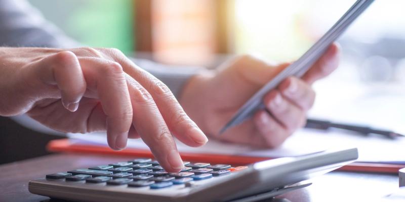 Close-up of hands using a calculator while holding a pen over paperwork