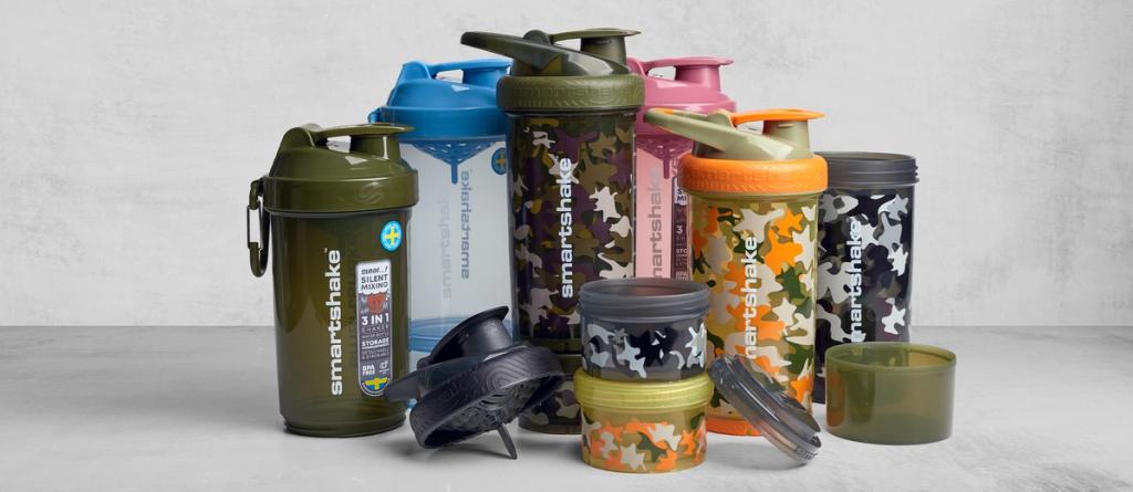 Group of Smartshake protein shaker bottles in green, blue, pink, orange and camo with storage containers