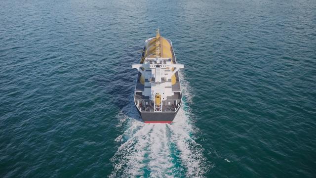 Aerial view of a cargo tanker ship sailing through open blue ocean, leaving a white wake behind it