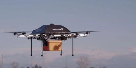 Amazon Prime Air delivery drone hovering outdoors carrying a small cardboard package