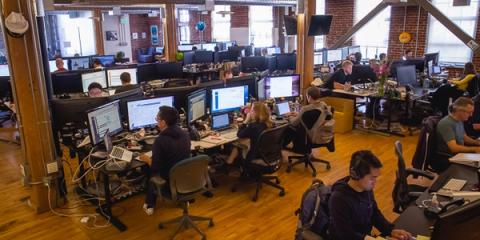 Open-plan office with employees working at desks of computer monitors in a loft with exposed brick and wood floors