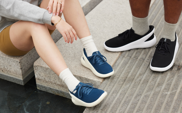 Two people sit on stone steps wearing blue and black Kizik slip-on sneakers
