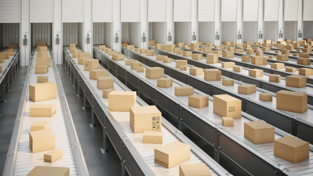 Rows of cardboard boxes traveling along conveyor belts in a large distribution warehouse