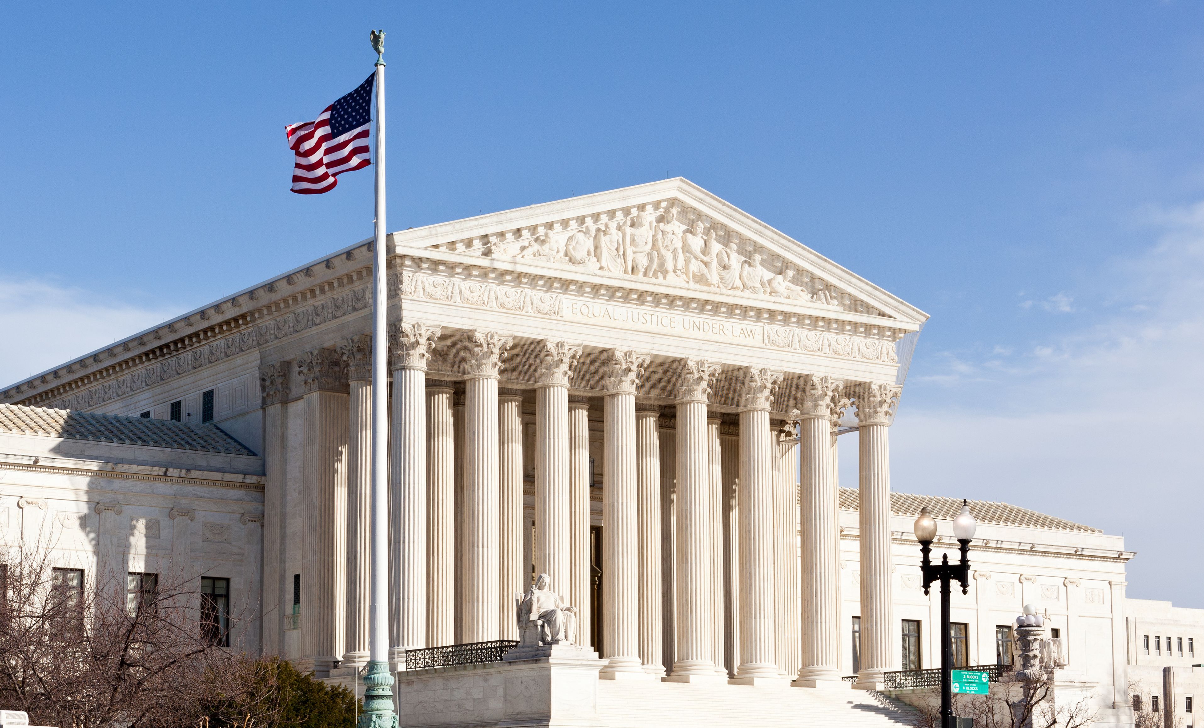 U.S. Supreme Court building with columns, "Equal Justice Under Law" inscription and American flag.