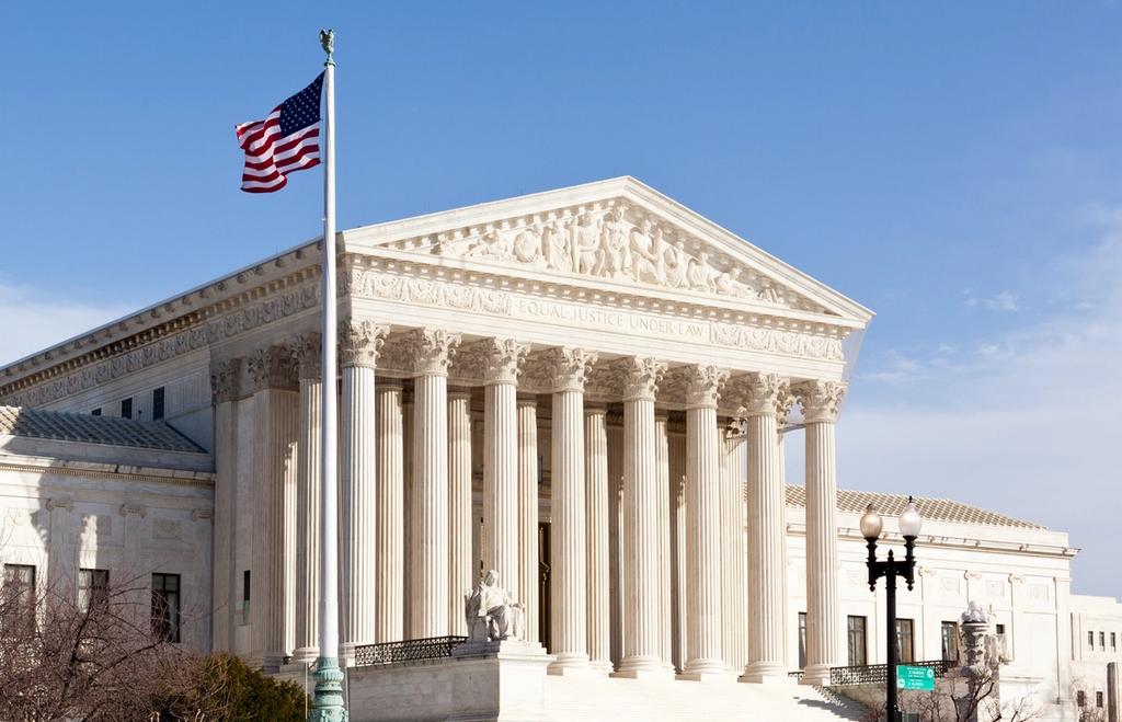 U.S. Supreme Court building with columns, "Equal Justice Under Law" inscription and American flag.