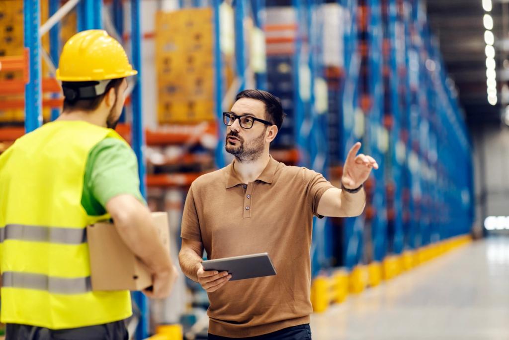 Two workers in a warehouse, one in hi-vis vest holding a box, the other in glasses holding a tablet and pointing