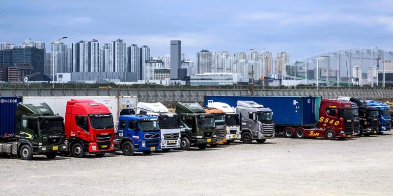 Row of colorful container trucks parked in a yard with a city skyline behind