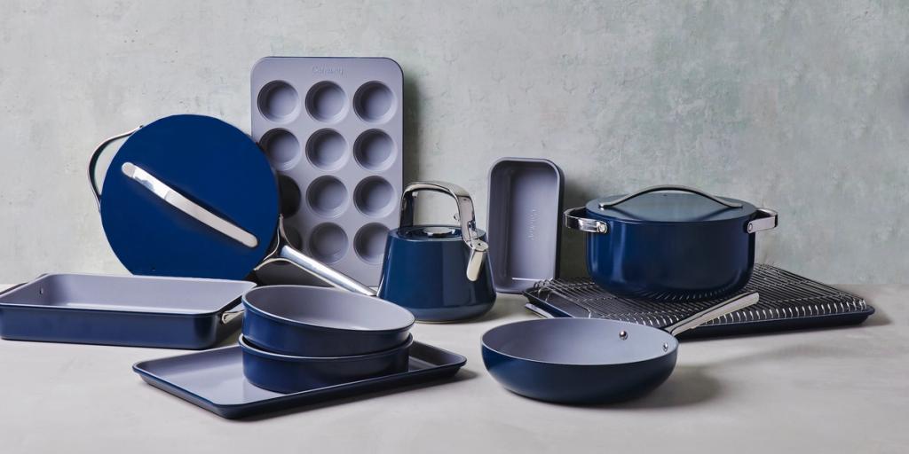 Navy and grey Caraway cookware set including pots, pans and a muffin tin on a grey surface