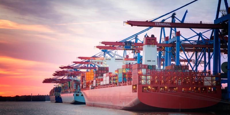 Container ships docked at a terminal with gantry cranes loading colorful containers at sunset