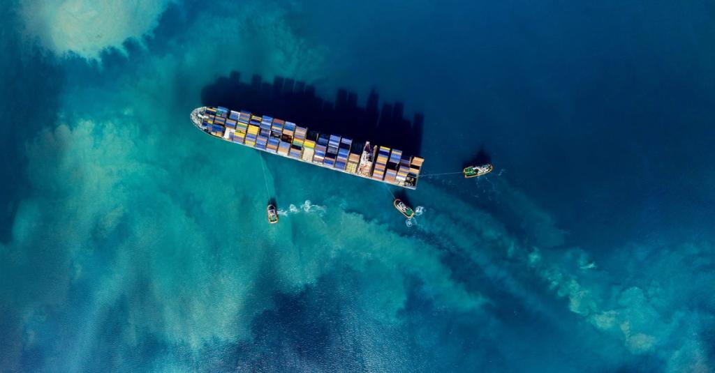 Aerial top-down view of a container ship escorted by tugboats over turquoise water