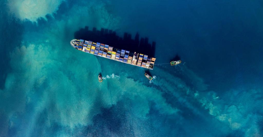 Aerial top-down view of a container ship escorted by tugboats over turquoise water