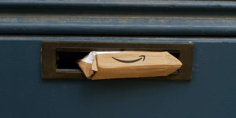 Brown Amazon-branded parcel with smile logo wedged in a blue door's brass letterbox slot