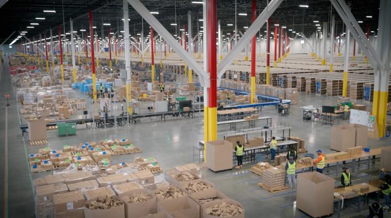 Vast fulfillment warehouse interior with workers in safety vests packing boxes among conveyor lines