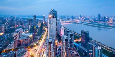 Aerial view of a dense Chinese city skyline with skyscrapers and a river bridge at dusk
