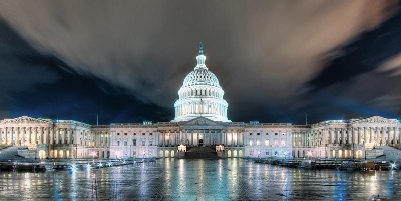 US Capitol building illuminated at night with reflections on wet plaza and dark clouds above
