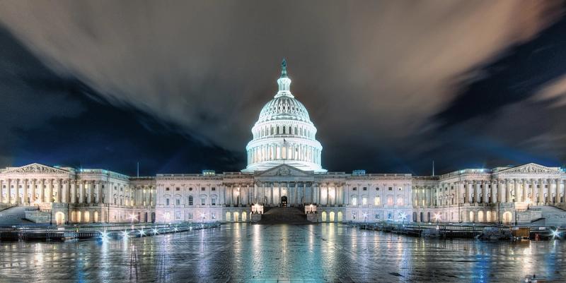 US Capitol building illuminated at night with reflections on wet plaza and dark clouds above