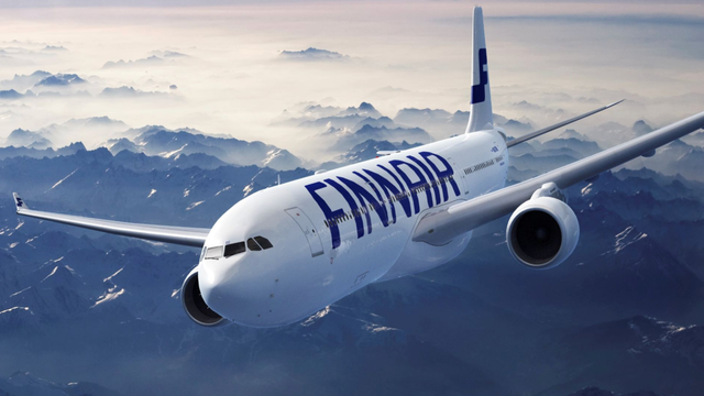White Finnair passenger jet in flight above snow-capped mountains under a blue sky
