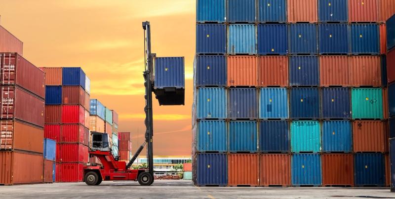 Reach stacker raising a container beside towering stacks of multicolored shipping containers at sunset