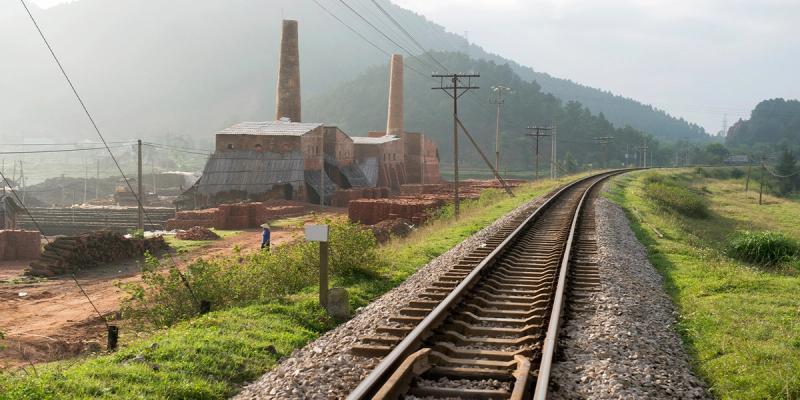 Brick kiln factory with tall chimneys beside a curving railway track through green countryside