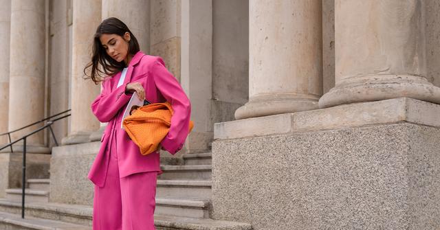 Woman in a pink suit holding an orange handbag walking down stone steps by tall columns