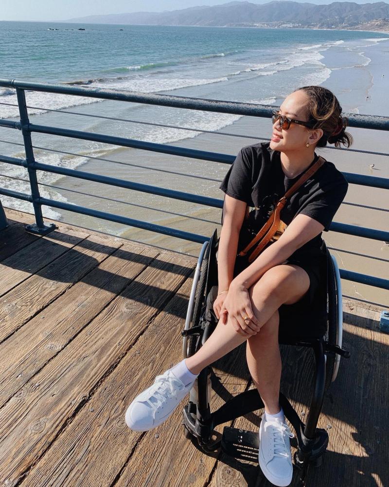 Person in a wheelchair wearing white Kizik sneakers relaxes on a seaside pier