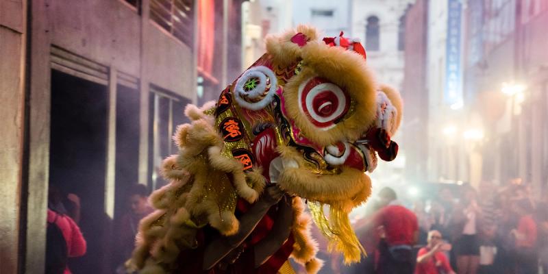 Performers carry an ornate gold and red lion dance costume through a smoky crowded street at night