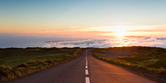 Empty highway curving toward a glowing sunset above a cloud-filled valley, evoking navigating a path through trade disruption.