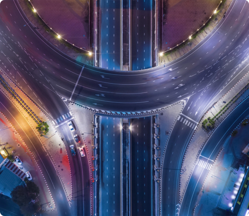 Overhead night view of an illuminated multi-lane highway interchange with overpasses and roundabout