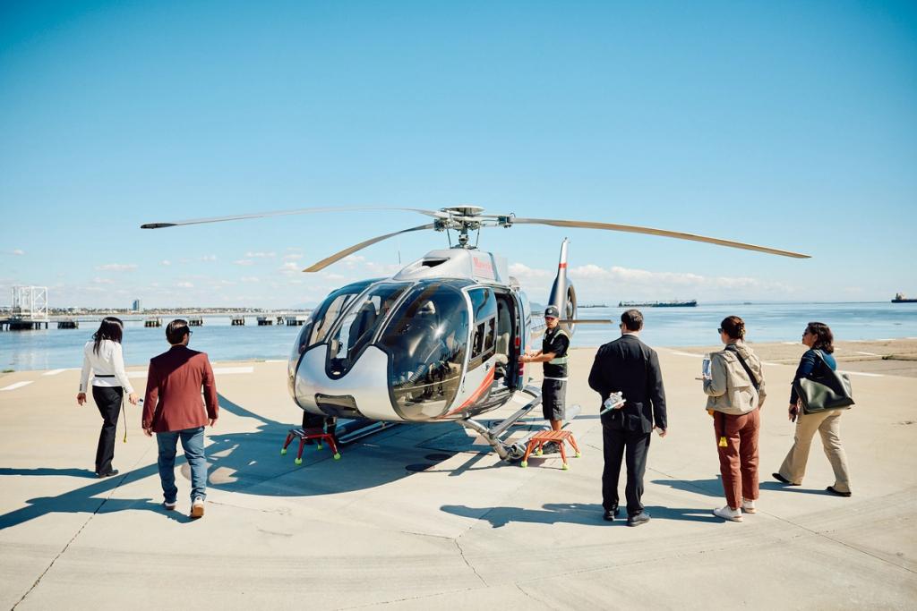 People in business attire walk toward a parked helicopter on a waterfront helipad under clear sky