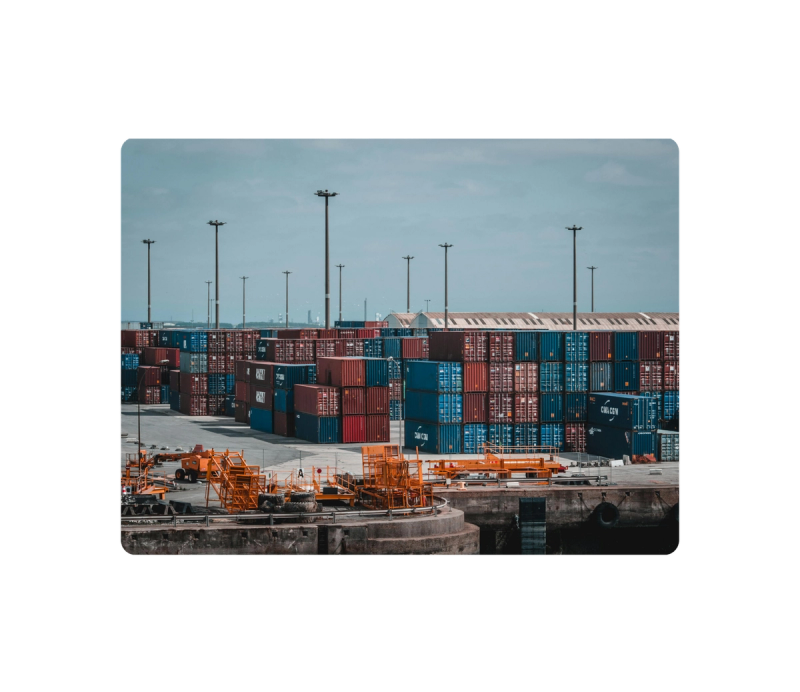 Stacked shipping containers and cargo handling equipment at a port terminal under an overcast sky