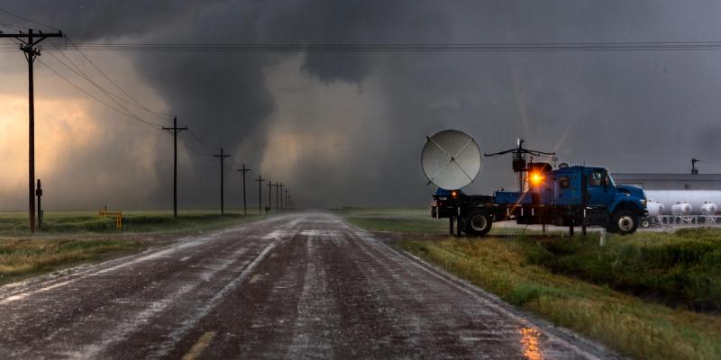 Storm chaser truck with a radar dish parked on a wet rural road as dark tornado clouds loom ahead