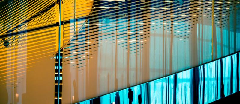 Silhouettes of people behind a backlit blue and amber glass architectural facade