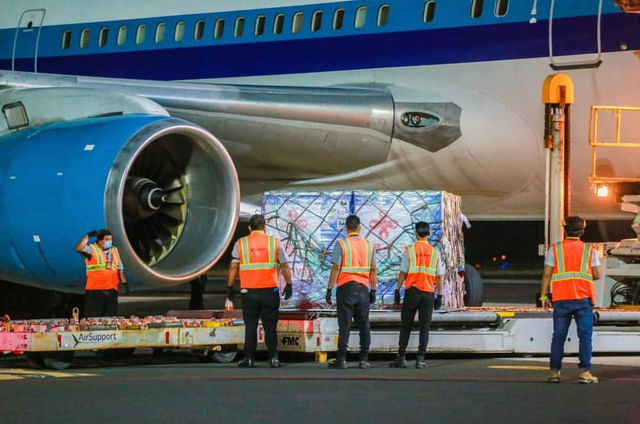 Ground crew in orange safety vests loading a pallet of cargo onto an aircraft at night