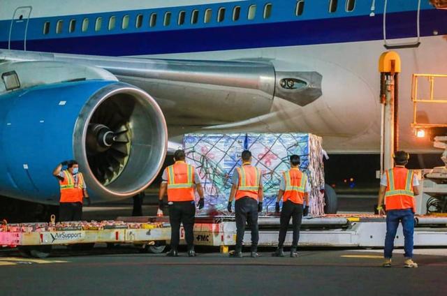 Ground crew in orange safety vests loading a pallet of cargo onto an aircraft at night