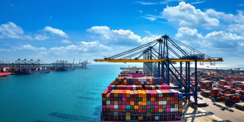 Aerial view of a container ship stacked with colorful containers beside cranes at a busy port
