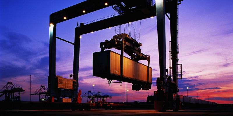 Port gantry crane lifting a shipping container at dusk under a purple and pink sky
