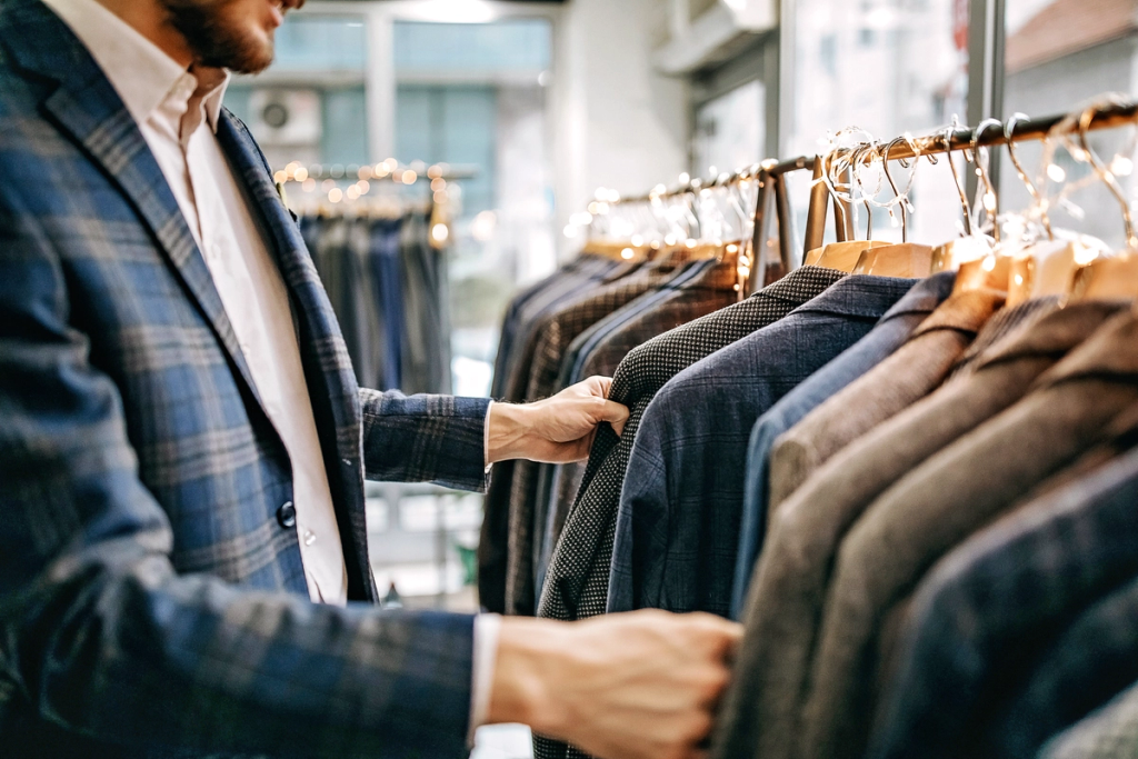 Man browsing clothing on hangers in a retail store.