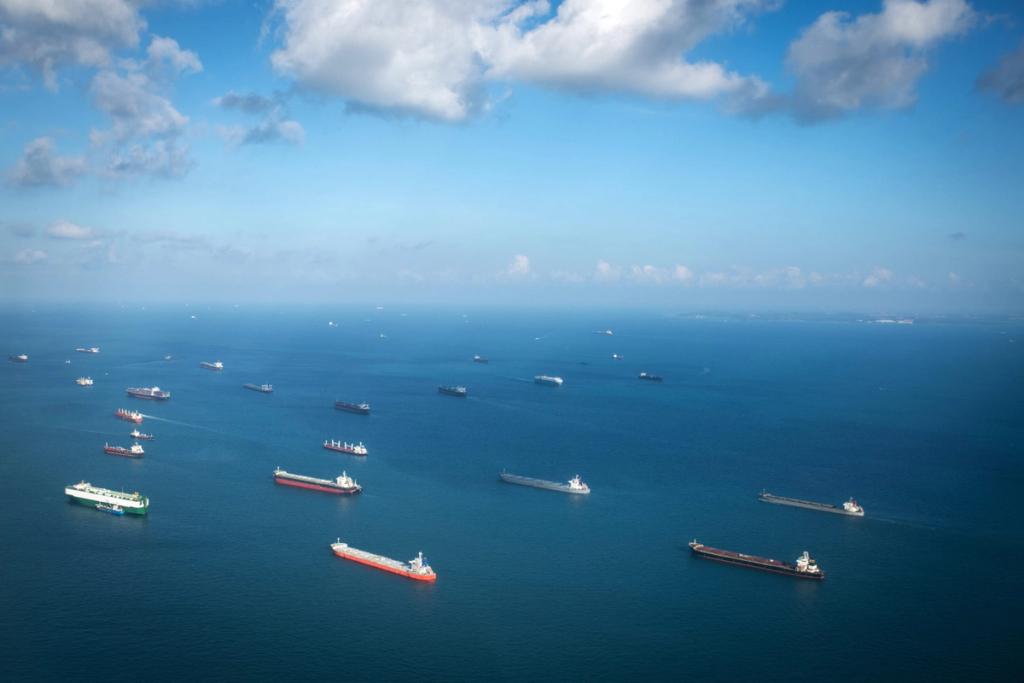 Aerial view of dozens of cargo ships and tankers anchored across blue open ocean under a partly cloudy sky