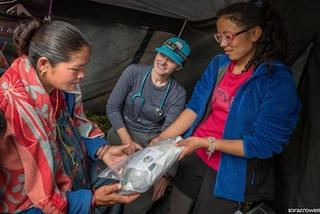 Three women in a tent examine clear plastic bags of medical supplies together