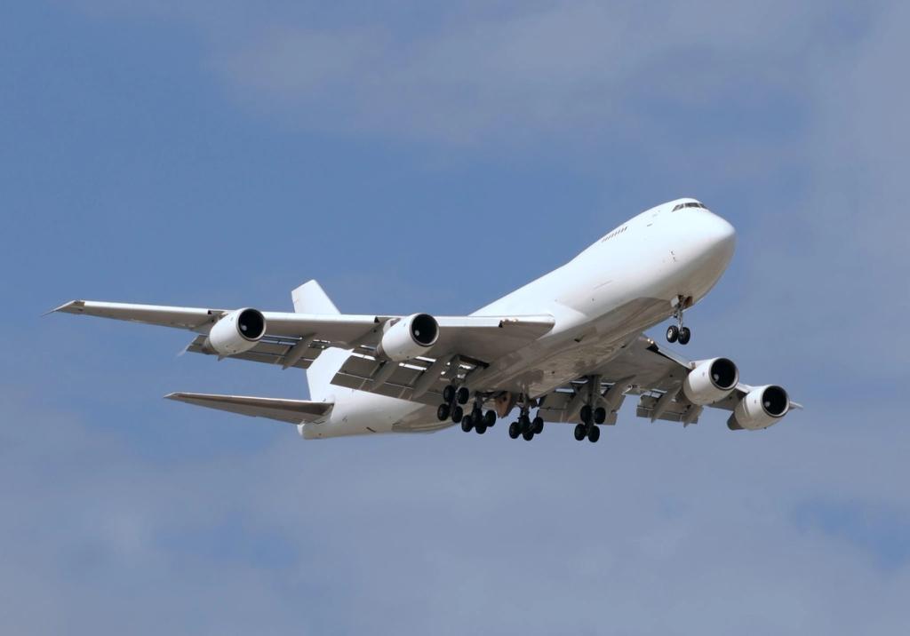 White four-engine Boeing 747 cargo jet on approach with landing gear down against a blue sky