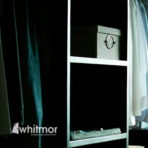 Dimly lit closet shelving with a fabric storage box and the Whitmor logo overlaid