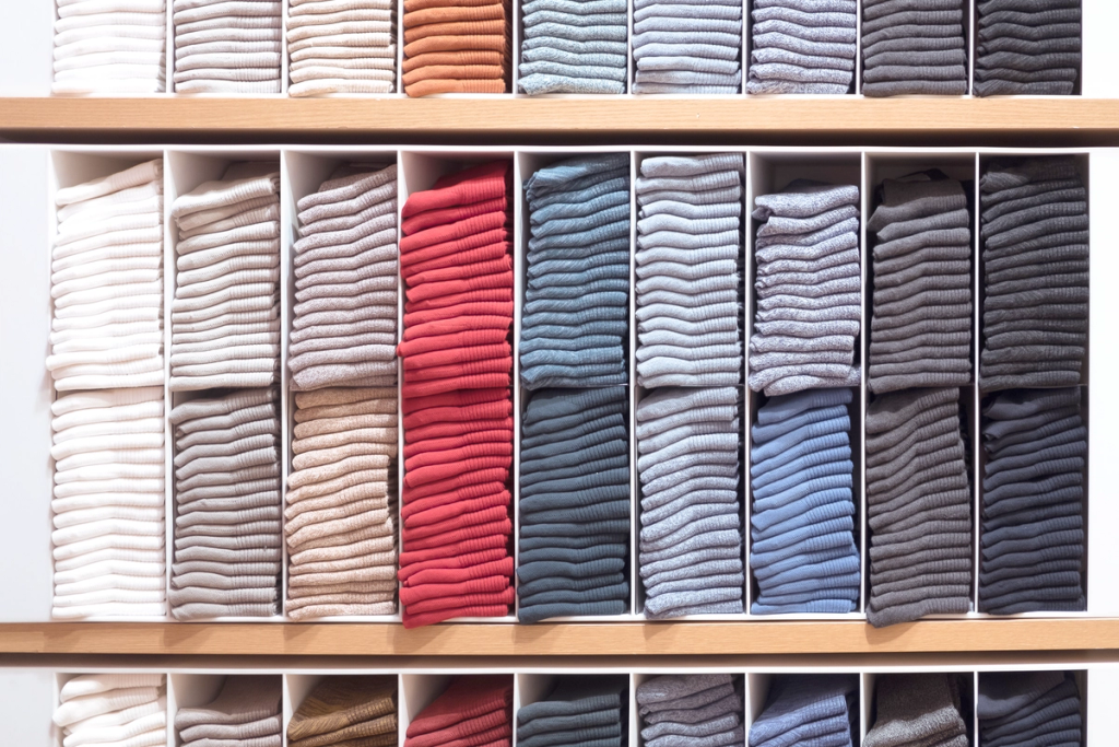 Neatly folded clothing items organized in compartments on wooden shelves.