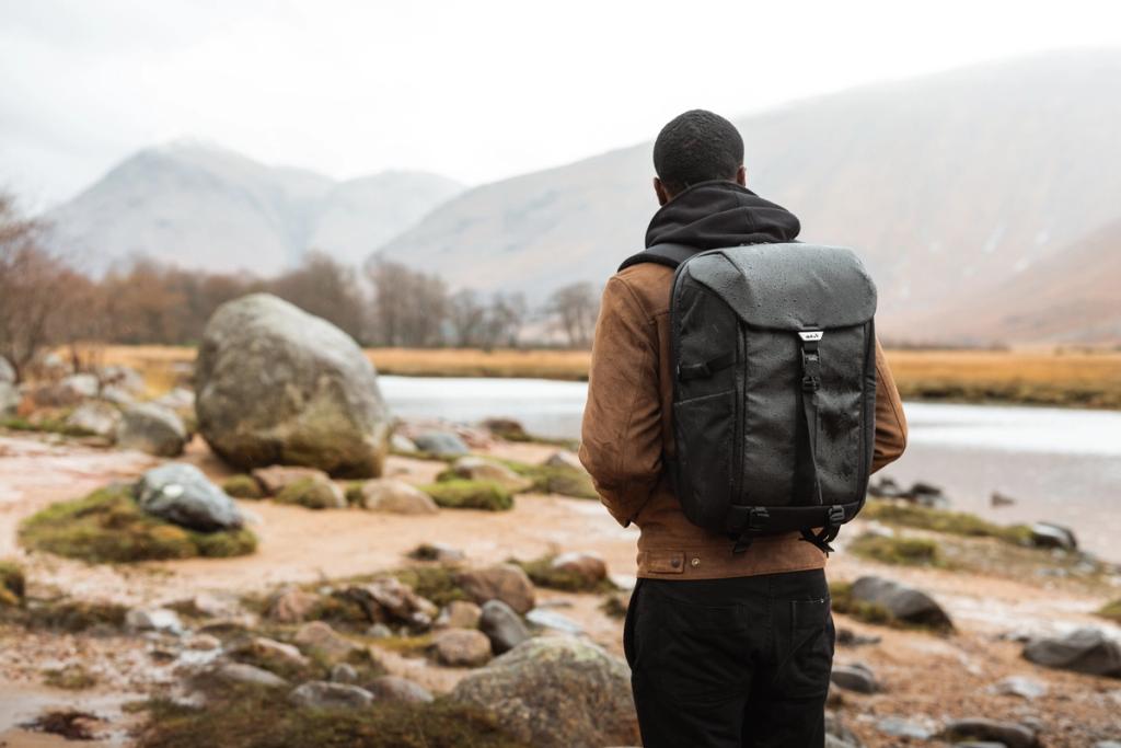 Man seen from behind wearing a black backpack looking out over a misty mountain landscape