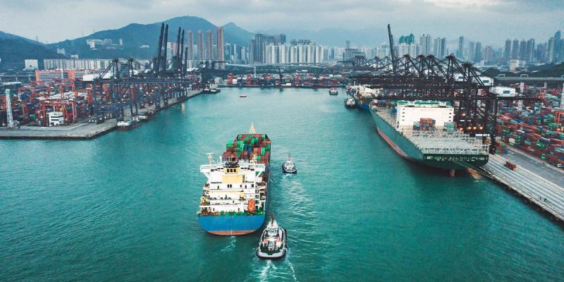 Aerial view of two container ships and tugboats moving through a busy harbor near a city skyline