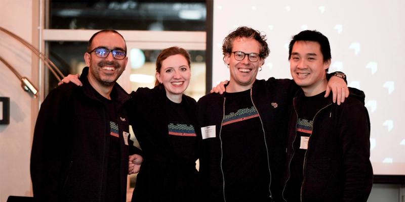 Four smiling colleagues in dark jackets pose arm-in-arm at an indoor launch event with Flexport arrow graphics behind