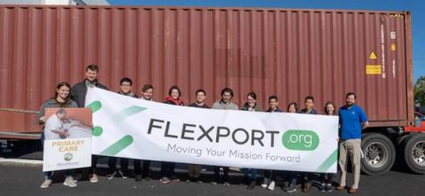 Group of people holding a Flexport.org Moving Your Mission Forward banner in front of a red shipping container