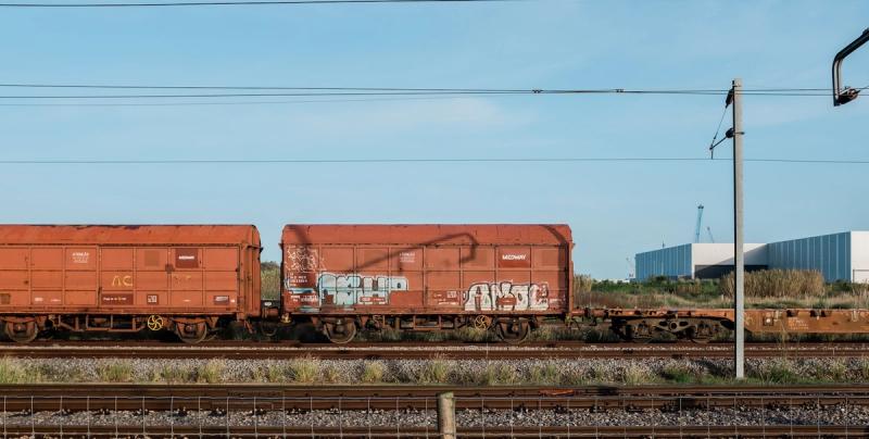 Rusty Medway freight rail wagons covered in graffiti parked on tracks near an industrial warehouse