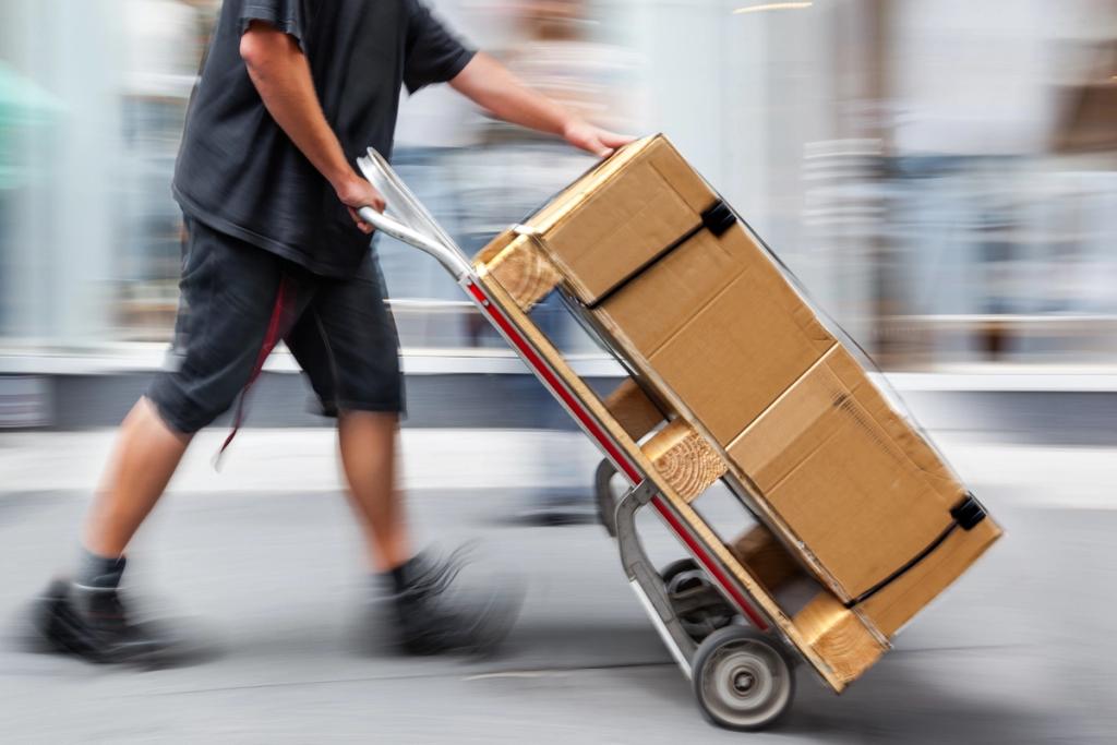 Delivery worker pushing a hand truck stacked with cardboard boxes while moving quickly.