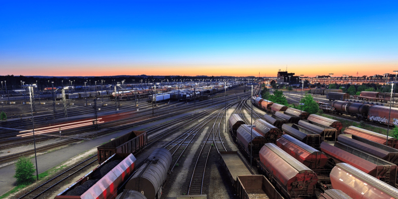 Wide view of a rail yard at dusk with many freight cars on converging tracks under an orange sky