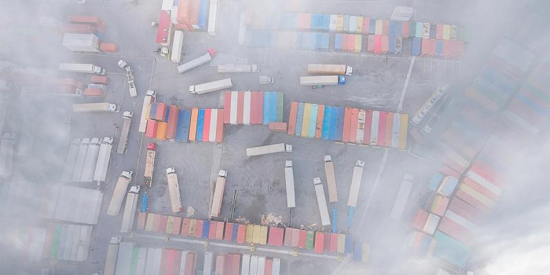 Aerial view of a container yard with truck trailers and stacked containers partly obscured by fog